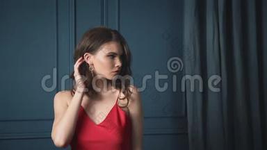 美丽的黑发女郎身着丝质红色礼服晚装靠在蓝色的墙壁上晒出奢华的生活魅力